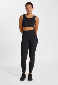 Svart sport-BH och högmidjade leggings set, tillverkade av stretchigt material. Har en liten röd logotyp på framsidan och sidan.