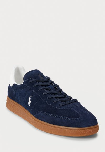 Tumesinine suede spordijalatsid valgete kandmistoonide aktsentidega, sidumisdisain ja kummine talla materjal. Küljel on tikandiga logo.