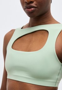 Κοντινό πλάνο ατόμου που φοράει αμάνικο crop top ανοιχτοπράσινου χρώματος με μεγάλο τετράγωνο άνοιγμα στο πάνω μέρος του στήθους.