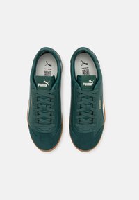 Sneaker in scamosciato e pelle verde scuro con lacci piatti, fodera morbida e suola in gomma. Presenta il logo Puma sulla linguetta.