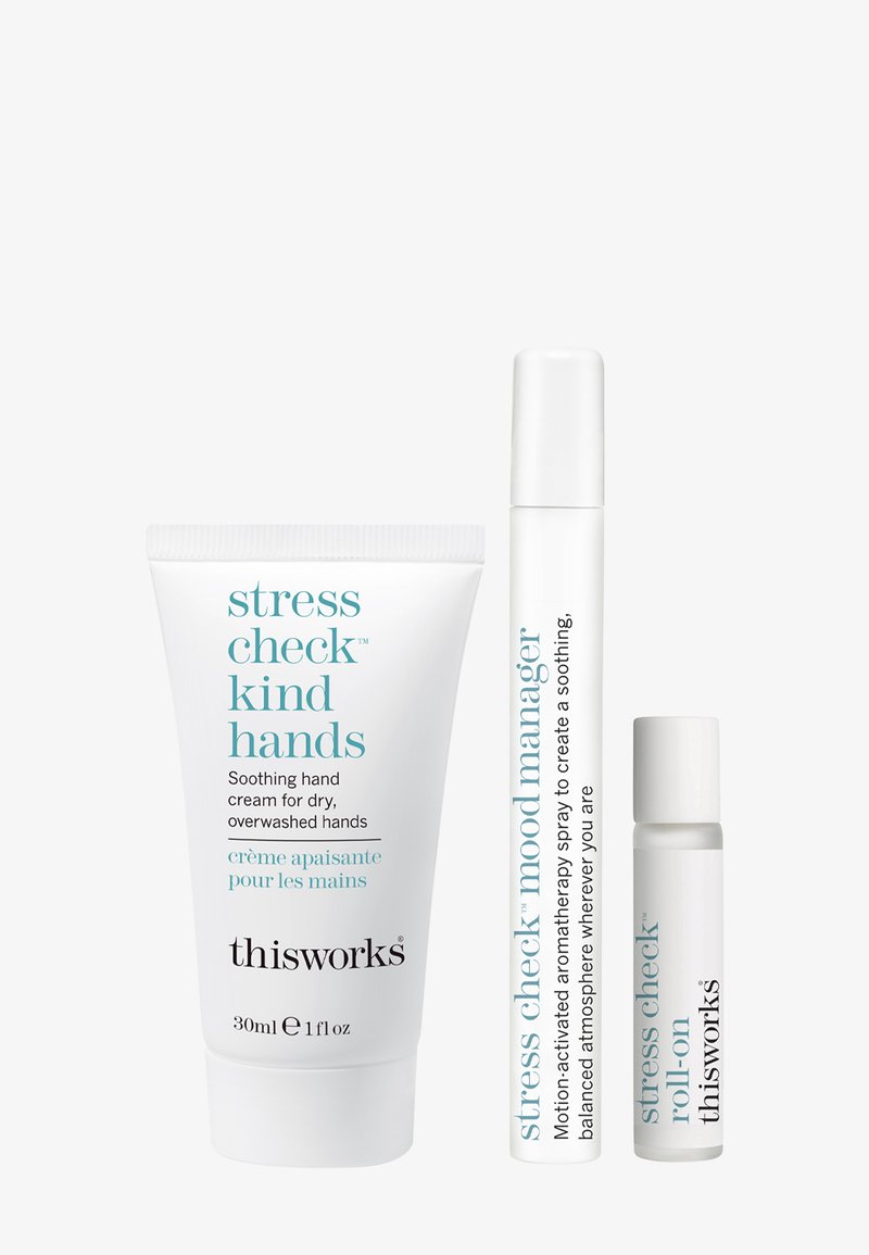 Set van drie thisworks-producten: witte tube handcrème, witte sprayfles, doorzichtige rol-on tube. Alle hebben een minimalistisch ontwerp en tekst.