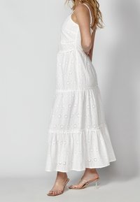 Vitt broderat maxi-klänning med ett lager på lager-design, justerbara spaghetti-axelremmar och en flödande nederkant. Bärs med genomskinliga klack-sandaler.