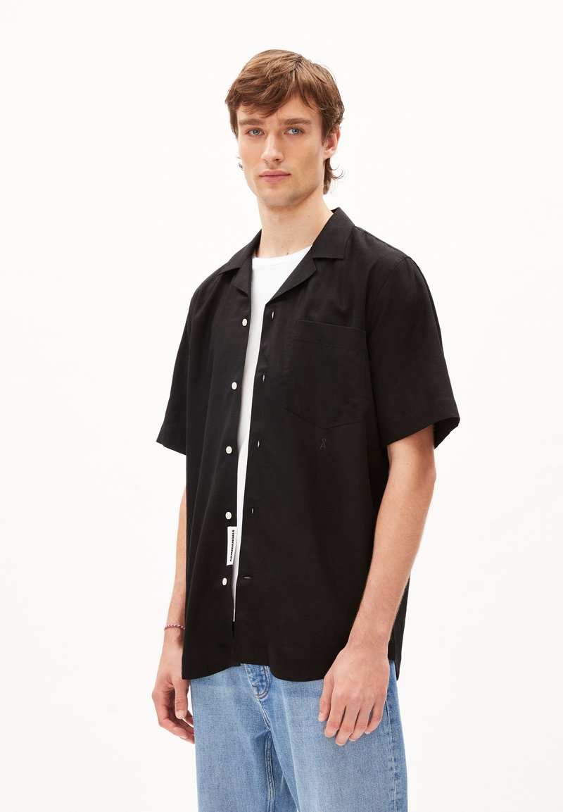 Zwarte korte mouwen shirt van zachte stof met een knoopsluiting aan de voorkant, puntcollar en een enkele borstzak. Te combineren met lichte jeans.