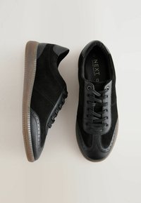 Svarta sneakers med mocka- och läderdetaljer, rund tå, snörningsdesign och en texturerad gummisula. Märkbar perforerad detaljering på sidorna.