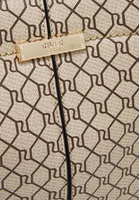 Sac à main beige à motifs géométriques marron, équipé d'une plaque logo River Island dorée et de coutures noires contrastantes.