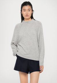 Vaaleanharmaa neulepaita, jossa on pyöreä pääntie, pitkät raglan-hihat ja ribba-helma, yhdistettynä tummansinisiinShortseihin.