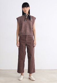 Brown sleeveless knit top with a ribbed hem, paired with high-waisted brown corduroy pants and white slip-on shoes. Decorative scarf around the neck.