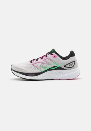 Zapatilla de correr ligera con un upper gris, acentos en rosa y verde, y una suela blanca gruesa con patrones texturizados, etiquetada como "Fresh Foam".