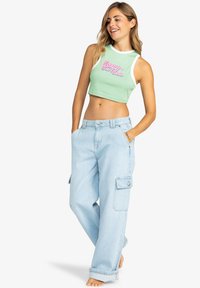 Top corto de color verde claro con ribete blanco y estampado "ROXY Surf Club", combinado con unos pantalones cargo holgados de color azul claro con bolsillos laterales.