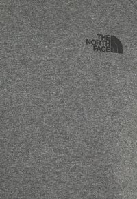 Felpa grigia realizzata in morbido misto cotone. Presenta un piccolo logo nero di "The North Face" nell'angolo in alto a destra. La texture è liscia.