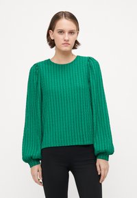 Green textured blouse with vertical stripes, puffed long sleeves, and a round neckline, paired with black fitted pants.