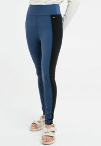 Mėlynos ir juodos sportinės leginsai su aukštu liemeniu, lygiu paviršiumi ir šoninėmis detalėmis. Derinami su šviesių spalvų sandalais su dirželiu.