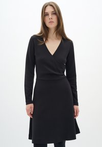 Abito lungo nero con maniche a lunga, scollatura a V, corpetto aderente e gonna a campana, realizzato in materiale morbido. Nessun motivo visibile o accessorio.