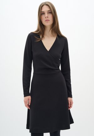 Vestido negro de manga larga con escote en V, cuerpo ajustado y falda acampanada, hecho de material suave. Sin patrones visibles ni herrajes.