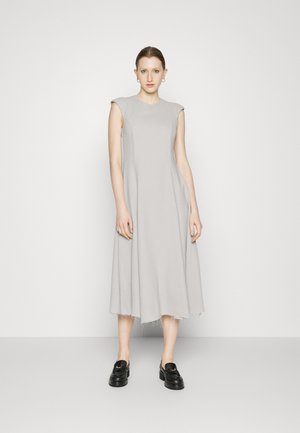 Vestido sem mangas de um tom cinza claro, com um corte descontraído, comprimento midi e bainha desfiada; combinado com sapatos de plataforma pretos. Textura do tecido suave.