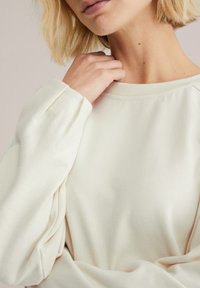 Hanorac crem deschis cu guler rotund, croială lejeră și mâneci adunate pentru un plus de textură. Material moale și neted, cu cusături minimale.
