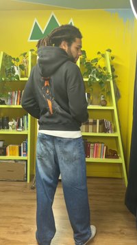 Sweatshirt preto com capuz e um desenho gráfico nas costas, com detalhes em laranja. Usado com jeans azuis desbotados e de pernas largas.