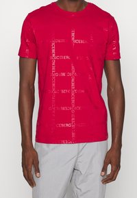 Rotes Baumwoll-T-Shirt mit Rundhalsausschnitt, das ein geprägtes Logo-Muster auf der Vorderseite in einer etwas dunkleren Farbe zeigt.