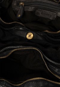 Interno di una borsa in pelle nera con un bottone a scatto in ottone, due compartimenti non zip, e una piccola etichetta in pelle con la scritta "Redesign EST. 2003."