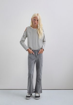 Camisa de manga larga a rayas con cortes en los hombros, combinada con jeans acampanados grises, que cuentan con bolsillos frontales y zapatillas con un patrón en blanco y negro.