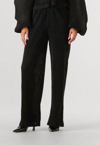 Zwarte geribde gebreide broek met een relaxte pasvorm, met een subtiele glans en licht uitlopende pijpen. Gecombineerd met puntige hoge hakken.