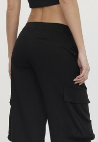 Zwarte cargo broek met zijzakken, een losse pasvorm en een textuurstof. De taille heeft riemlussen en een tailleband voor verstelbare maten.