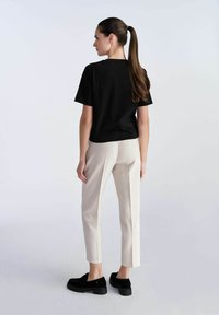 Czarna bawełniana koszulka, luźny krój, zestawiona z beżowymi spodniami w kant, z bocznymi rozcięciami, oraz czarnymi butami typu slip-on, widok z tyłu.