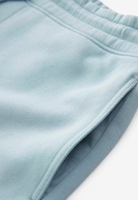 Pantaloni jogger azzurri chiari realizzati in morbido tessuto con una superficie liscia, dotati di una vita elastica e tasche laterali. Dettagli delle cuciture visibili.