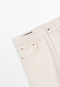 Cremeweiße Denim-Jeans, die die obere Vorderseite mit Knopfverschluss, Gürtelschlaufen und genieteter Fronttaschen-Detail zeigen.