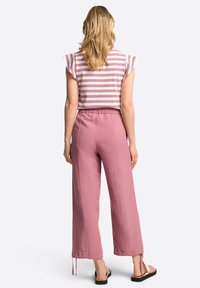 Randig kort topp med ärmar, kombinerad med rosa vida byxor. Materialet verkar lätt, med en avslappnad passform och dragsko-detaljer.