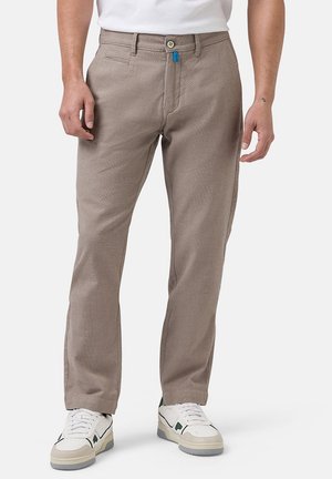 Beige, strukturierte Hose mit schlanker Passform. Verfügt über einen Knopfverschluss, Fronttaschen und einen blauen Akzent am Bund. Ein Paar weiße Sneakers.