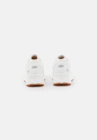 Par de zapatillas blancas Skechers con suelas marrones mostradas desde atrás sobre un fondo gris claro liso.