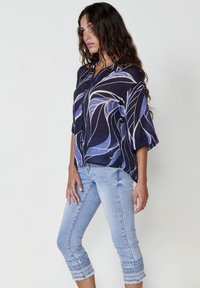 Blusa blu navy con motivi a foglia bianca e blu, maniche corte e design con bottoni. Abbinata a jeans cropped azzurri con orli ricamati.