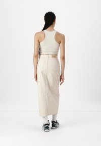 Beige cargo skjørt laget av bomull med sidelommer, lengde til midt på leggen. Kombinert med en lys tank topp og svarte joggesko.