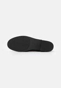 Suela de un zapato de vestir negro con agarre texturizado, tacón rectangular y la marca "MICHAEL KORS" cerca del área del dedo del pie. Talla marcada 7 ½ M.