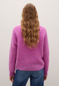 Maglione rosa in misto mohair con un pattern testurizzato, polsini a costine e una vestibilità cropped. Abbinato a jeans di denim blu.