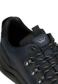 Schwarze Ledersneaker mit strukturiertem Design, flachen Schnürsenkeln, verstärkten Ösen und gepolsterter Schuhkragen. Mit einem Zugschlaufe an der Ferse.