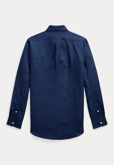 Camisa azul marino de manga larga con botones, mostrada desde atrás con un pliegue central en la espalda y puños abotonados sobre un fondo blanco.