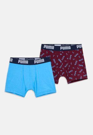 Twee paar Puma boxershorts, één effen lichtblauw en één donkerrood met blauwe Puma-logo's, beide met een marineblauwe elastische tailleband.