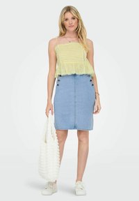 Light yellow sleeveless top with stripes and eyelet trim, paired with a denim skirt featuring button detailing on the side and white sneakers.