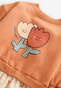 Sweatshirt avec deux tulipes souriantes, l'une beige et l'autre de couleur rouille, avec des tiges vertes et le texte « BEST DAY » sur le côté.