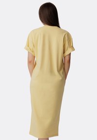Żółta bawełniana sukienka T-shirtowa z podwiniętymi rękawami, do kolan, luźny krój, gładka faktura i wycięcie na plecach; minimalistyczny design.