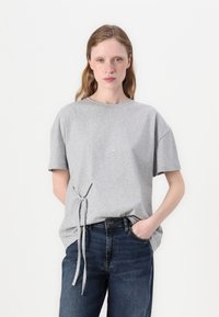 Gray short-sleeve T-shirt with a round neckline and side tie detail, made of soft fabric; paired with dark blue denim jeans.
