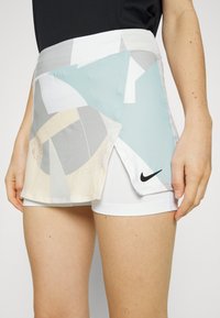 Falda deportiva para mujer de Nike con un overlay de patrón abstracto en tonos pastel, banda elástica en la cintura y pantalones cortos blancos interiores. Acento del logotipo negro en el dobladillo.