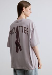 Oversized lavender t-shirt featuring dark maroon graphic text "PIROUETTES" and ballet shoes on the back. Soft fabric with short sleeves.