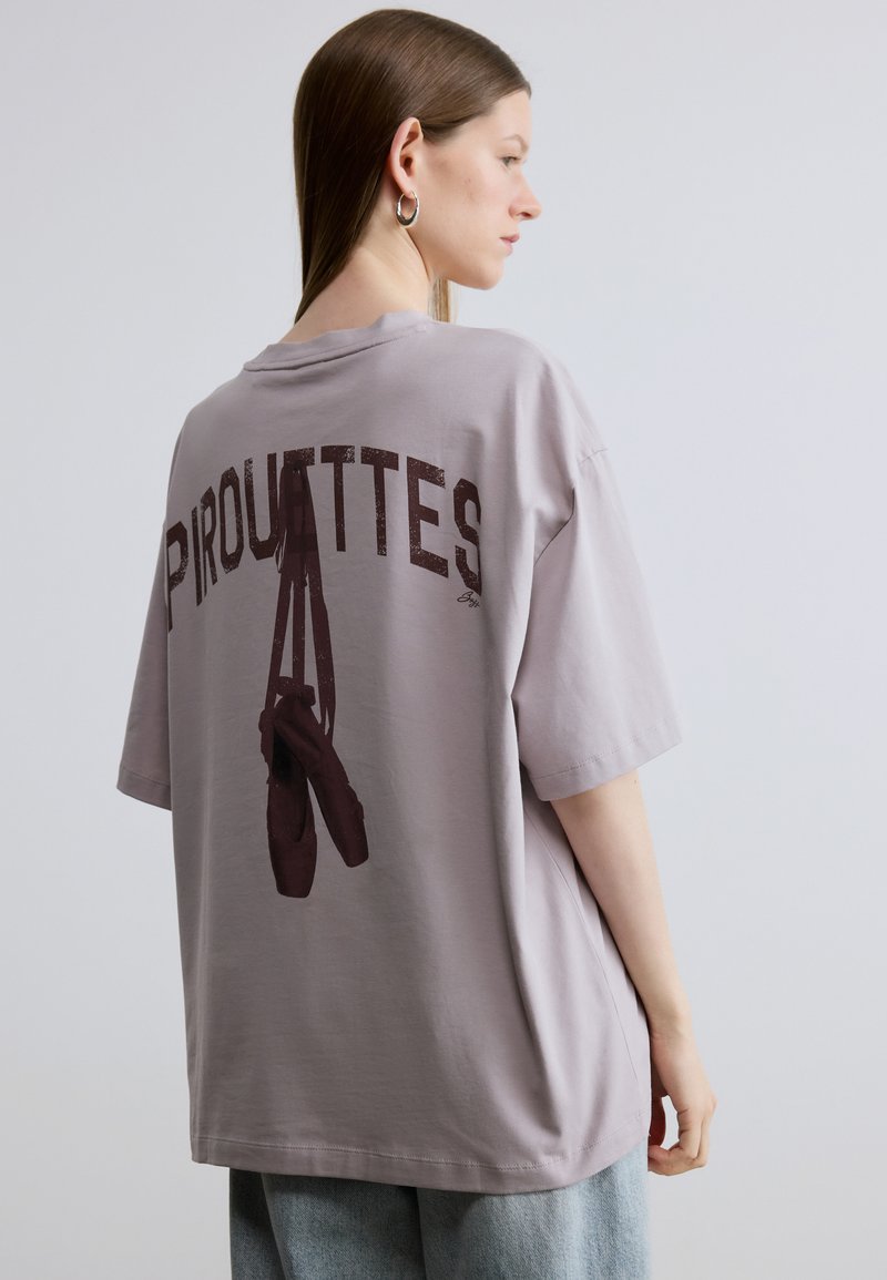 Oversized lavender t-shirt featuring dark maroon graphic text "PIROUETTES" and ballet shoes on the back. Soft fabric with short sleeves.