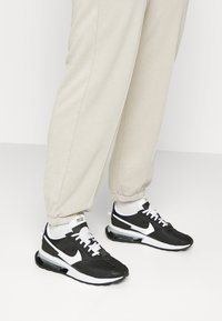 Svart och vit Nike-sneakers med textilövre, stoppad krage och synlig luftdämpning. Kombinerat med ljusbeige joggers.