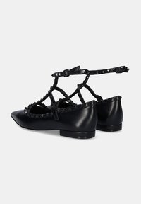 Bailarinas de cuero negro con punta afilada, correas entrecruzadas y tachuelas en forma de pirámide a lo largo de los bordes. Tacones sólidos bajos para mayor soporte.