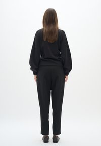 Black sweatshirt with voluminous sleeves and a ribbed hem, paired with tailored black trousers. Smooth texture, casual design, minimal detailing.