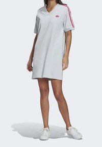 Lichtgrijze sportjurk met V-hals, korte mouwen en roze strepen. Voorzien van een logo op de borst en een relaxte pasvorm.